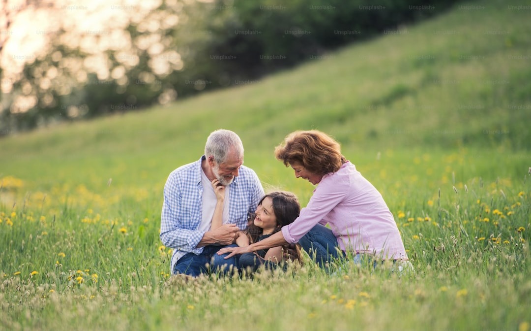 Grandparents and granddaughter laugh together in a field of wildflowers.